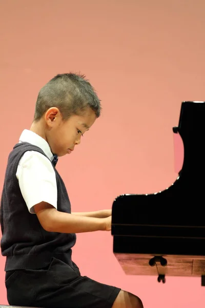 Japansk pojke spela piano (första klass i grundskolan) — Stockfoto