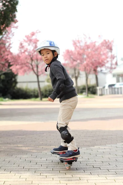 日本男孩骑着 casterboard （就读小学一年级) — 图库照片