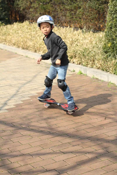 Japanischer Junge reitet auf einem Casterboard (erste Klasse der Grundschule)) — Stockfoto