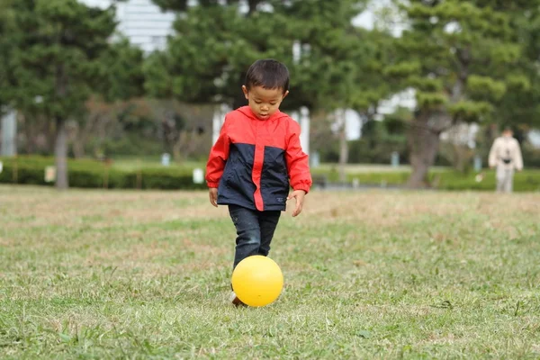 Japonês menino chutando uma bola amarela (3 anos de idade) na grama — Fotografia de Stock