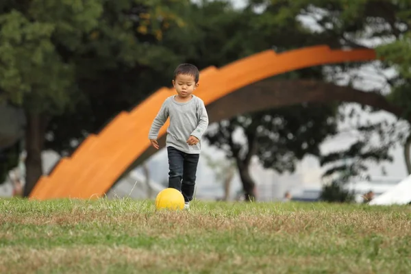 Japonês menino chutando uma bola amarela (3 anos de idade) na grama — Fotografia de Stock