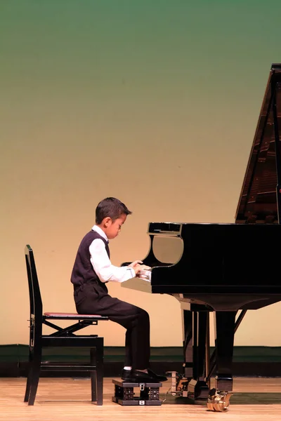 舞台でピアノを弾く日本の少年 (小学校 2 年生) — ストック写真