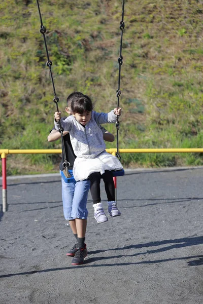 日本人妹オンザスイングと弟プッシュ彼女の背中 10歳の男の子と5歳の女の子 — ストック写真