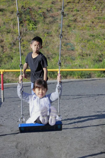 日本人妹オンザスイングと弟プッシュ彼女の背中 10歳の男の子と5歳の女の子 — ストック写真
