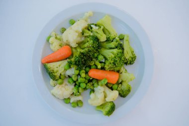 Pişmiş salata, havuç, bezelye, Brüksel lahanası beyaz tabakta.