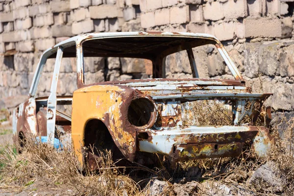 Verlaten en roestige skelet van een Sovjet-Russische auto langs de kant van de buitenkant van het gebouw — Stockfoto