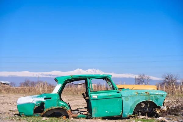 Verlaten wrak van een oude groene Sovjet-Russische auto in het midden van de droge landbouwgrond in zuidelijke Armenië Stockfoto