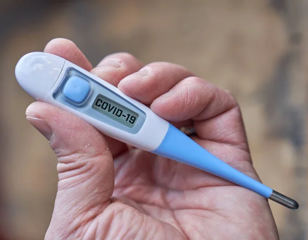 Male hand holds clinical thermometer with covid-19 text on the screen during global covid-19 or corona pandemic