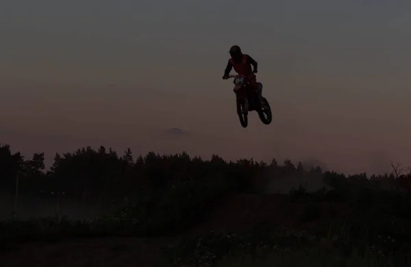 Verschwommene Silhouette eines Motocross-Fahrers, der im Sonnenuntergang auf den Berg springt — Stockfoto