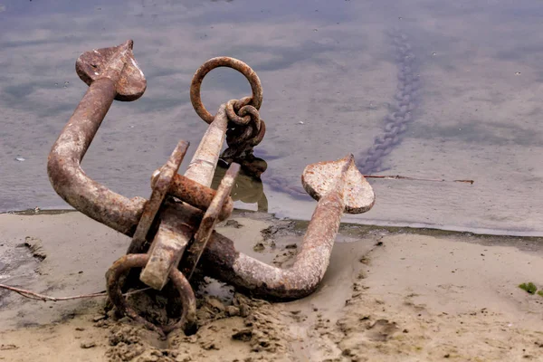 RUSTY ANCHOR WET BEACH SAND AND WHITE SEA-WAVE FOAM — Stock Photo, Image