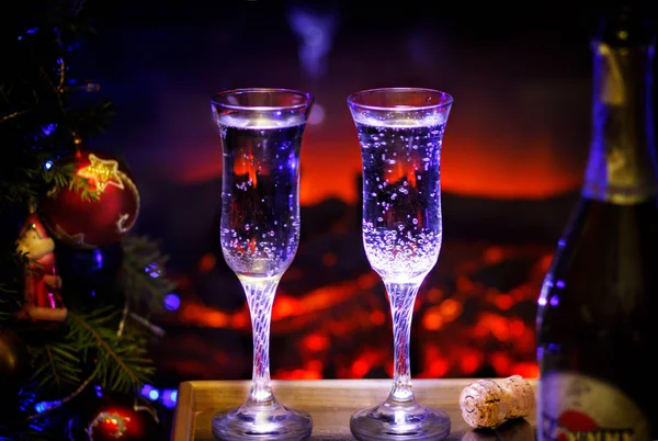 Two glasses of sparkling champagne in front of warm fireplace. Cozy relaxed magical atmosphere in a chalet house by the fireside. Snug holiday concept. — Stock Photo, Image