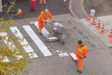 Trafik çizgisi boyama. İşçiler yaya geçidinde beyaz sokak çizgileri çiziyorlar. Arka planda turuncu ve beyaz çizgili yol konileri, yol inşaatı sırasında asfalt üzerinde duruyorlar