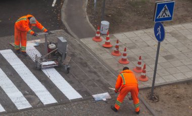 Trafik çizgisi boyama. İşçiler yaya geçidinde beyaz sokak çizgileri çiziyorlar. Arka planda turuncu ve beyaz çizgili yol konileri, yol inşaatı sırasında asfalt üzerinde duruyorlar