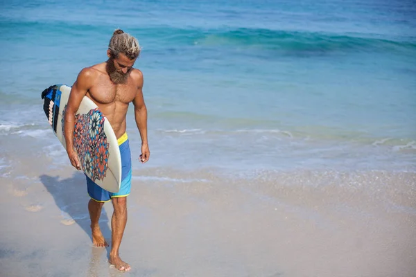 Porträt eines attraktiven, bärtigen, lockigen Mannes mit Surfbrett am Strand, der sich auf der linken Seite des Rahmens befindet — Stockfoto