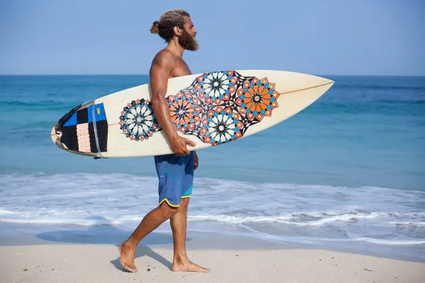 Ganzkörperporträt eines attraktiven bärtigen, lockigen Mannes mit Surfbrett, der an einem Strand spaziert — Stockfoto