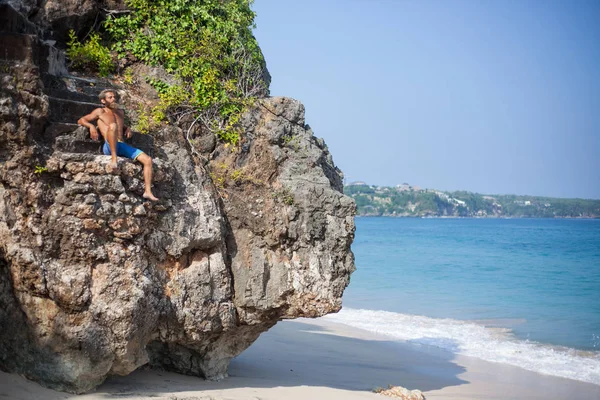 Retrato panorámico horizontal de un atractivo hombre barbudo sentado en una roca cerca del océano — Foto de Stock