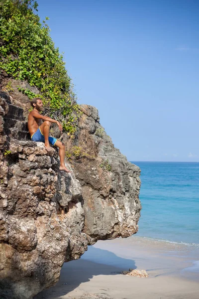 Retrato vertical de un atractivo barbudo sentado en una roca cerca del océano — Foto de Stock