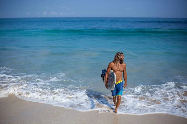 Horizontales Porträt eines attraktiven bärtigen lockigen, nassen Mannes mit Surfbrett, der aus dem Ozean kommt und nach rechts schaut — Stockfoto