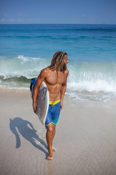 Vertikales Porträt eines gutaussehenden bärtigen lockigen, nassen Mannes mit Surfbrett, das aus dem Ozean kommt und nach rechts schaut — Stockfoto