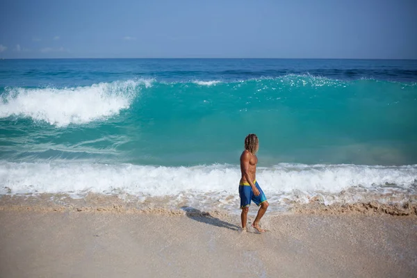 Attraktiver muskulöser blonder Mann steigt aus dem Meer und blickt auf die große Welle, die hinter ihm aufsteigt — Stockfoto