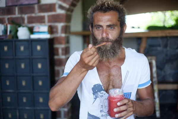 Attractive bearded curly man with a mug of smoothie is sitting in a cafe and eating the ice-cream