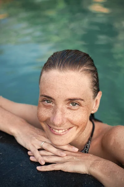 Retrato vertical de cerca de una hermosa chica con pecas y cabello mojado en el agua, brazos en el borde de la piscina — Foto de Stock