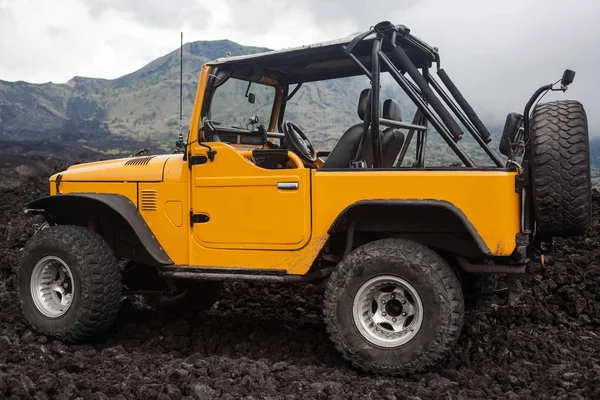 Offroad yelow vehicle parked at the top of a valley with volcanic rock and mountains in Bali, Indonesia