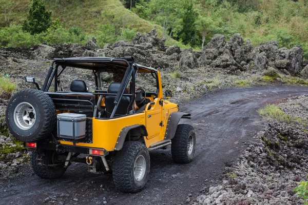 Sarı offroad araç arka görünümü yeşil ağaçlar arasında koyu zemin ile bir yolda bir sürücü tarafından tahrik edilmektedir.