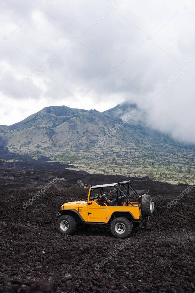 Offroad yelow vehicle parked at the top of a valley with volcanic rock and mountains in Bali, Indonesia