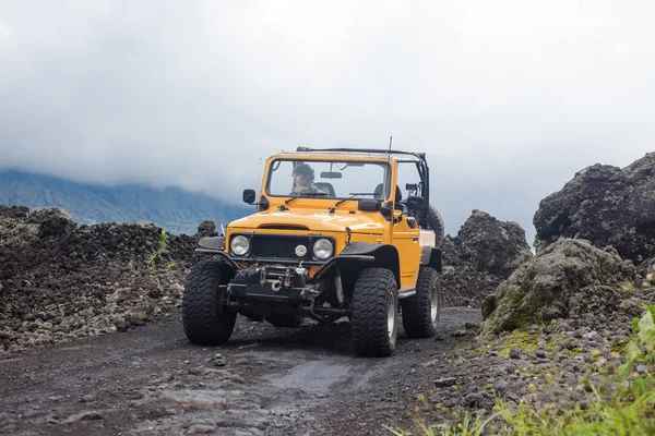 A curly-haired man is looking away driving an offroad yelow vehicle at the top of a valley with dark ground road — Stock Photo, Image