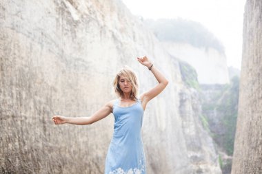 Yatay açık mavi elbiseli çekici bir kız portresi Dağları ile gözleri kapalı ve el sidewards arasındaki yolda duruyor