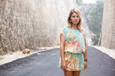 Yatay çiçekler ve soyut Yazdır ve tüy küpe ile elbiseli çekici bir sarışın kız portresi dağlar arasındaki yolda duruyor