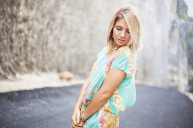 Yatay yakın çekim portre sarışın kız elbise soyut baskı ile kapalı gözlerle dağlar arasındaki yolda duruyor