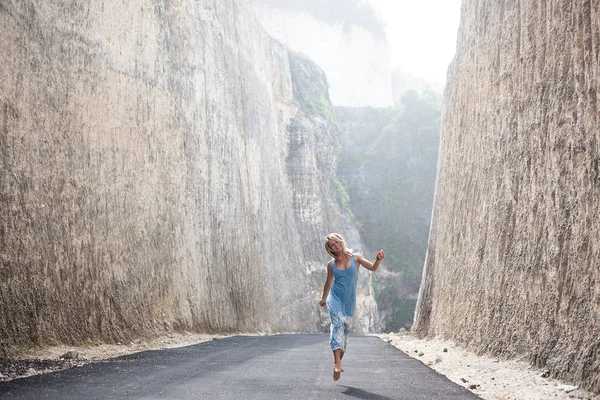 Feliz hermosa chica sonriente en vestido azul claro está saltando en el camino entre las montañas — Foto de Stock