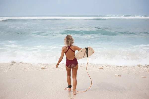 Horizontální panoramatické portrét atraktivní surf dívky v plavkách tmavě červená, je jít do oceánu s surfovací prkno, pohled zezadu — Stock fotografie