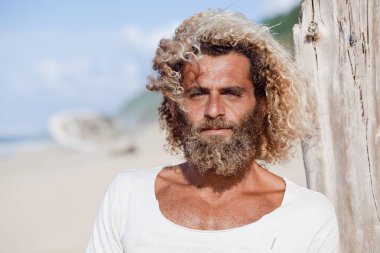 Robinson Crusoe. Portrait of curly-bearded man on the beah with a ship wreckage on the background. clipart