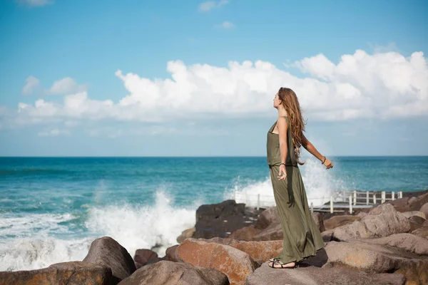 Chica joven se para en una playa de piedra cerca de las olas del mar — Foto de Stock