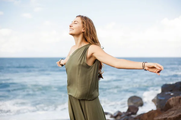 Young smiling girl stands with spread arms on stone beach close to the sea waves — Stock Photo, Image