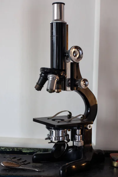 vintage old black metal microscope on table. white wall is in backgraund