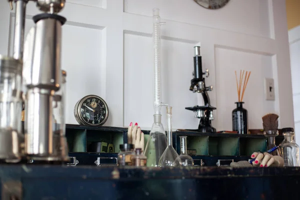 식탁 위에 오래 된 빈티지 물건을 올려 놓고. 유리 플라스크와 시험관, 복강경 현미경, 화살이 달린 오래 된 둥근 자명종, 마네킹 손 — 스톡 사진