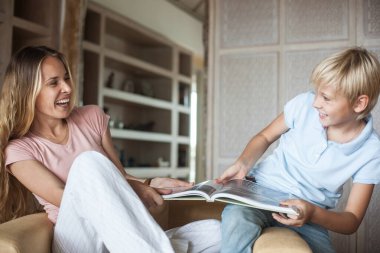 Genç, güzel bir anne ve genç bir oğlan koltukta otururken eğleniyorlar. Bir kadın ve bir genç kız kitap çekiyor ve gülüyorlar. sarışın aile.