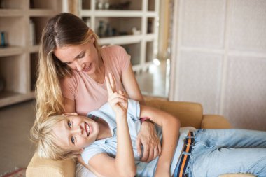 Kanepede genç oğluyla kucak kucağa oturan güzel bir anne. Mutlu gülümseyen sarışın aile