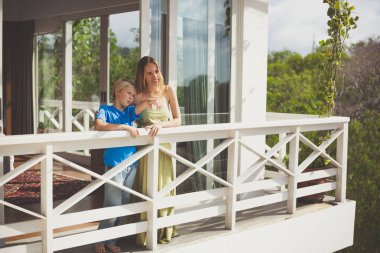 Karantina, tecrit, evde kalmak. Genç ve çekici bir kadın ve genç oğlu beyaz camdan bir evin balkonunda dikiliyorlar ve uzaklığa bakıyorlar. Yaz, güneşli gün