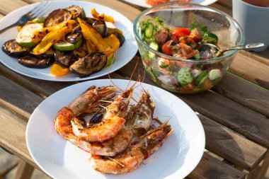 Beyaz tabakta ızgara Langoustines ve sebzeler, bahçedeki ahşap masada taze salatayla dolu bir kase. Yaz zamanı.