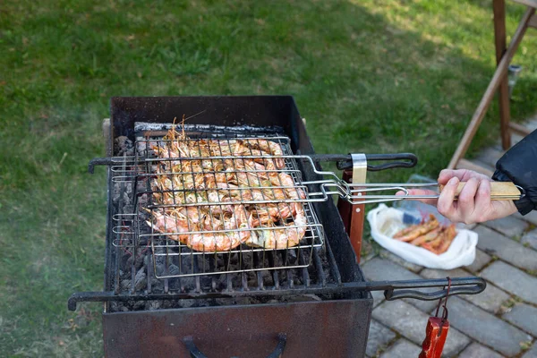 Langostinos grandes de color rosa con caparazón se encuentran en la parrilla con humo. Barbacoa al aire libre. Primavera. Mano masculina sostiene la parrilla — Foto de Stock