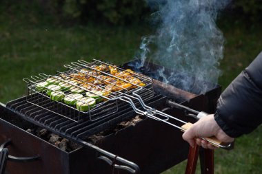 Erkek el ızgarayı kabak dilimli ve sarı dolmalık biberli açık hava dumanlı barbekü ile tutuyor.
