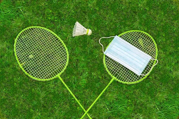 コロナウイルス保護シンボル バドミントンのラケットと緑の芝生の上でシャトルチェック 1つのラケットの医療用マスク 上からの眺め 禁止されている — ストック写真