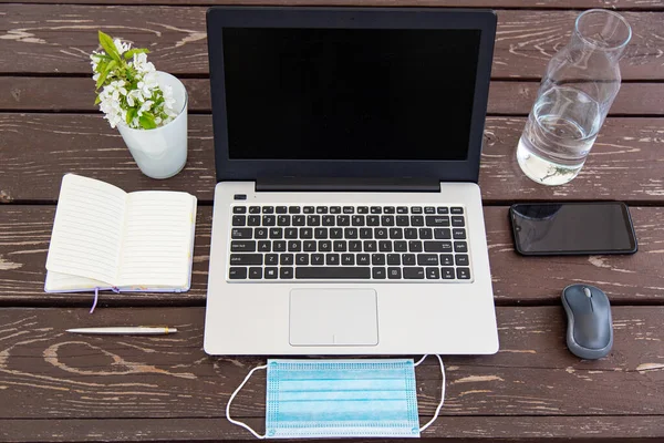 distant work or study from home during the coronavirus pandemic. Medical mask, laptop, mouse, notepad, mobile phone on a brown wooden table