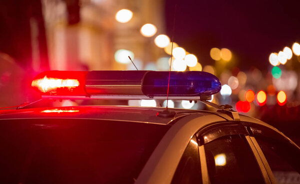 Red light flasher atop of a police car. City lights on the background. 