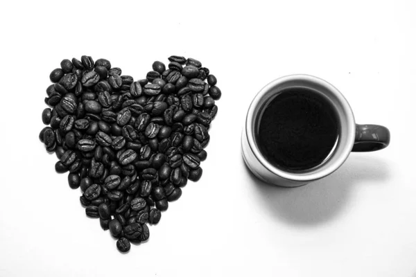 Forme de coeur créé avec des grains de café et une tasse — Photo